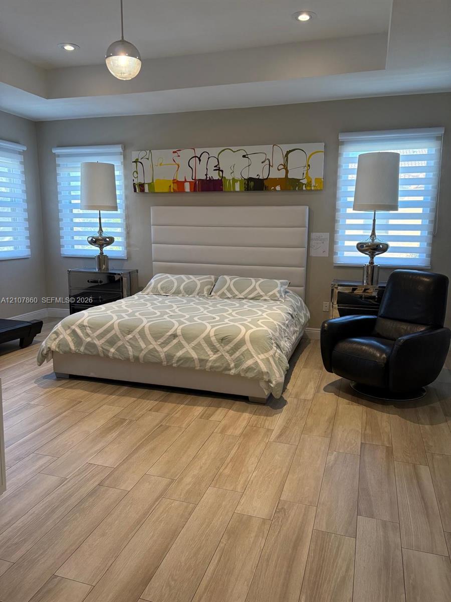 Tray ceiling featuring recessed lighting, wood-finish flooring, and dual windows with motorized roller shades