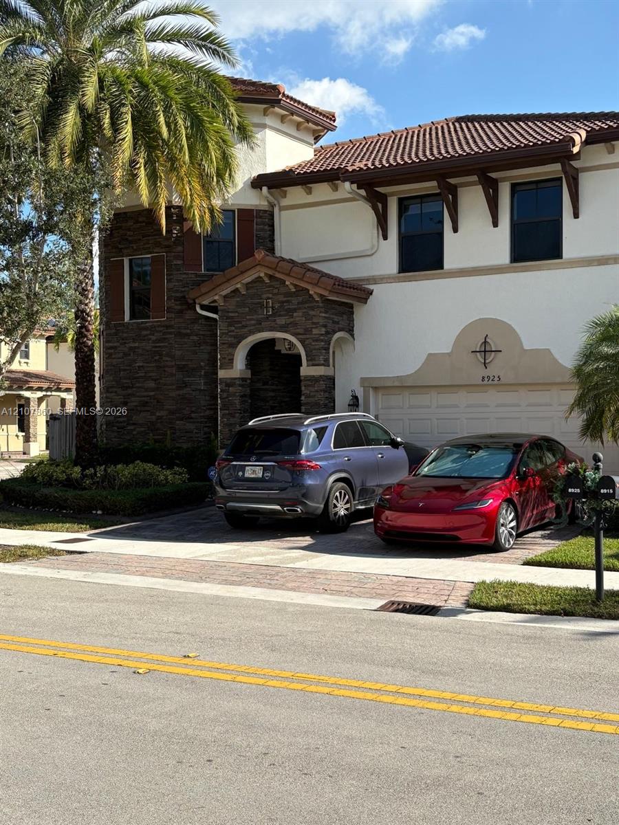 Stucco exterior featuring decorative stone veneer masonry, tiled roof with exposed rafter tails, and paver driveway