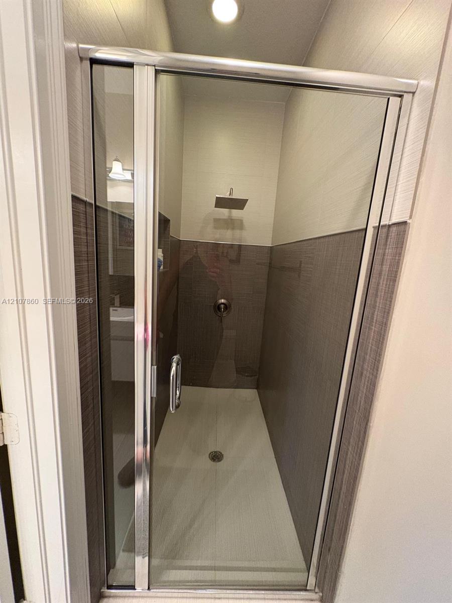 Walk-in shower featuring a glass enclosure with a silver-finish frame, a square rainfall showerhead, integrated wall niche, and two-tone horizontal tile surround