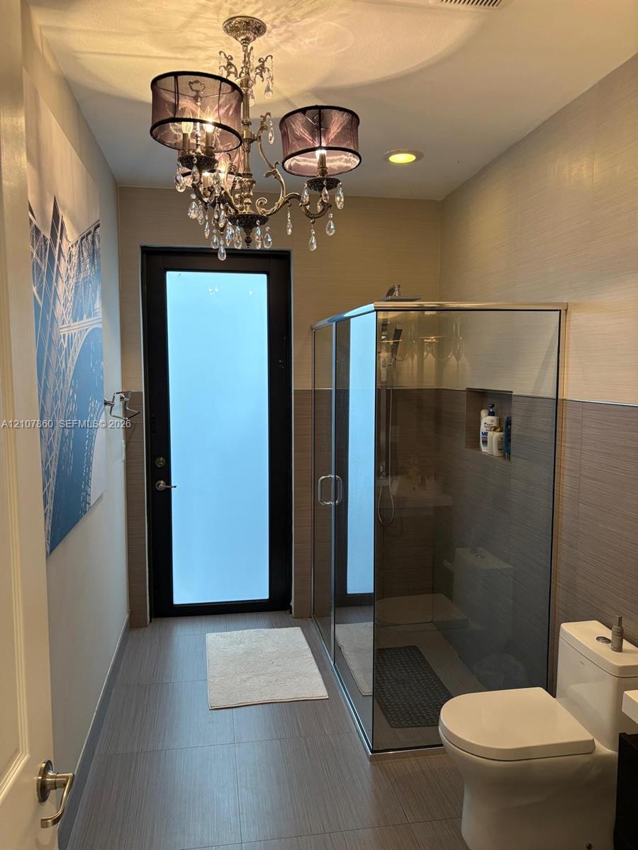 Bathroom featuring a walk-in glass-enclosed shower with a recessed wall niche, dual-tone tiled wall finish, frosted-glass exterior door, and ornate crystal chandelier lighting