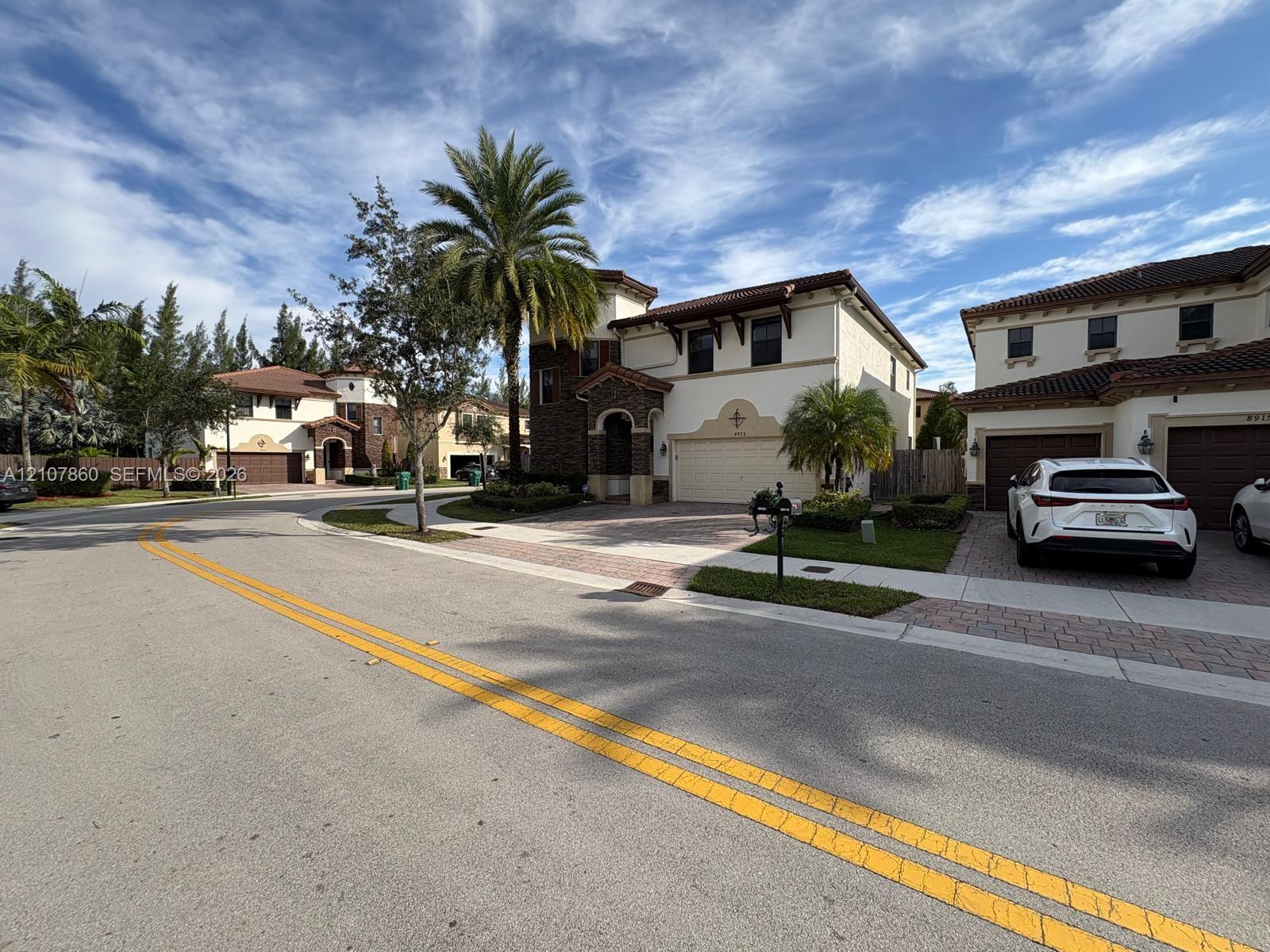 Two-story exterior featuring a stucco facade with decorative stone accents, a tiled roof, paver driveway, and an attached multi-car garage
