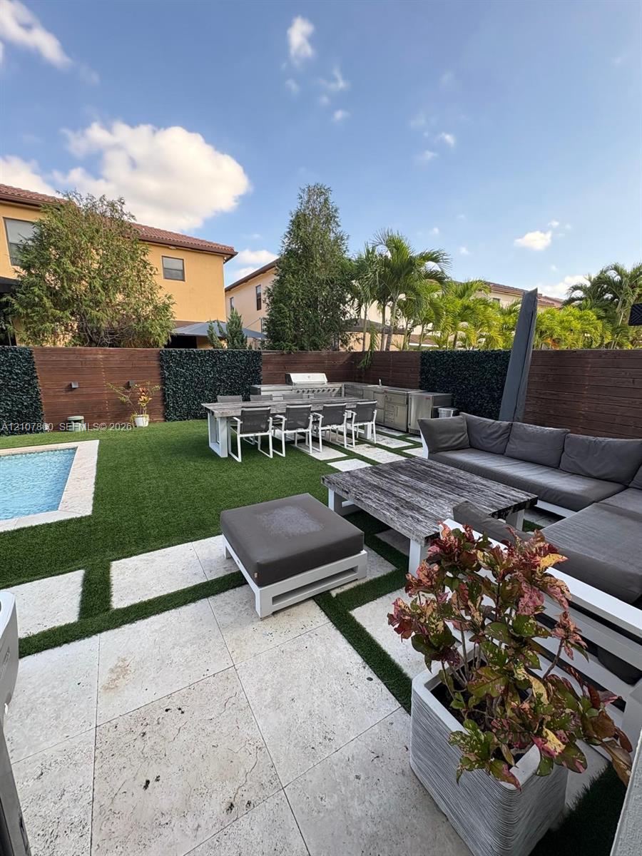 Backyard area featuring a swimming pool, stone paver decking with grass inlay, built-in outdoor kitchen, and tall privacy fencing