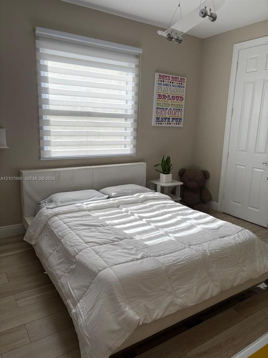 Neutral-toned room featuring wood-finish flooring, a multi-panel door, installed ceiling-mounted track lighting, and a roller shade window treatment