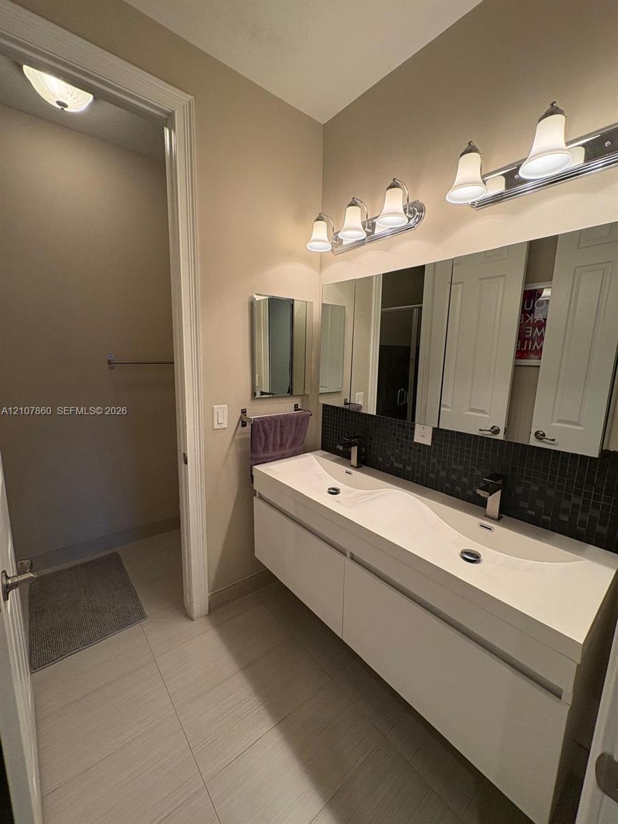Floating dual-sink vanity with a seamless integrated basin, dark mosaic tile backsplash, large wall-mounted mirror, and multi-bulb polished chrome vanity lighting