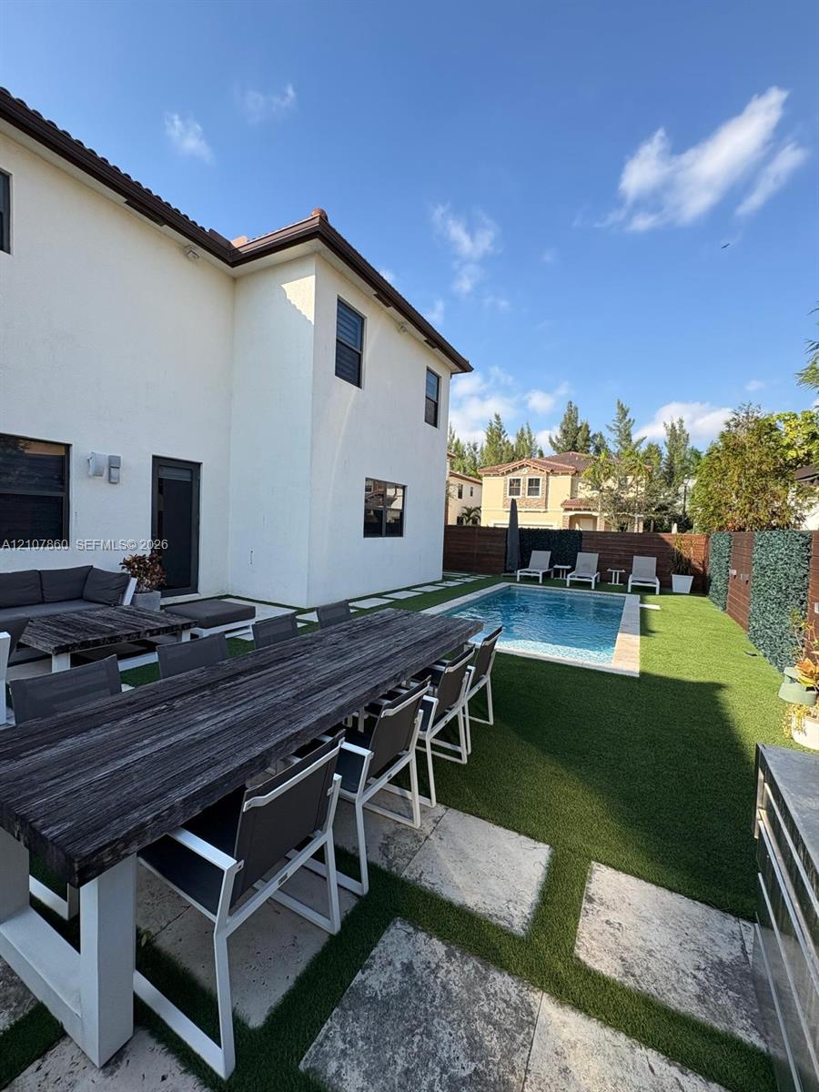 Backyard featuring an in-ground swimming pool, synthetic turf lawn, stone paver accents, and perimeter privacy fencing