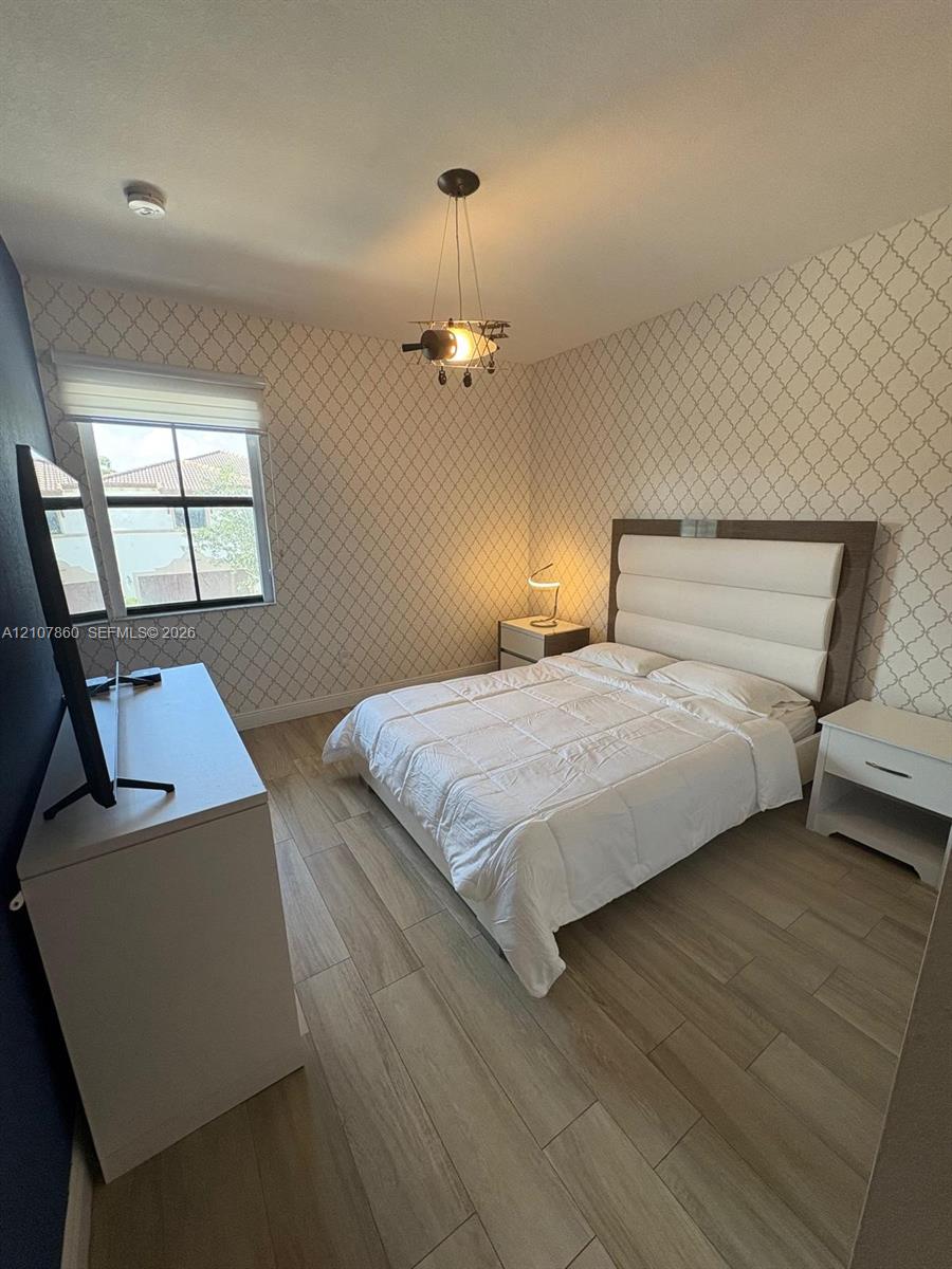 Room featuring patterned wall covering, wood-finish flooring, and a multi-light pendant fixture