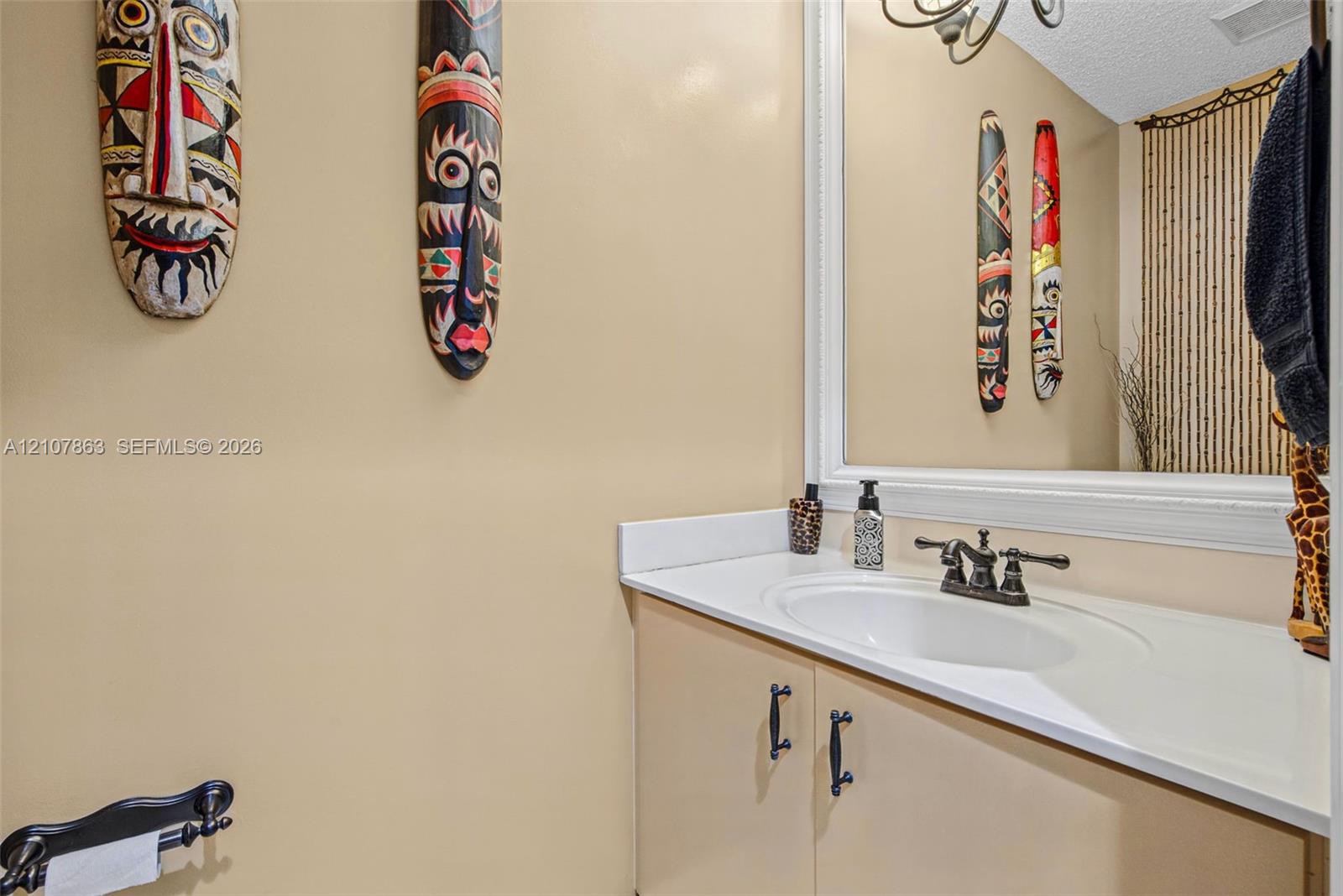 Bathroom vanity featuring a solid-surface countertop with an integrated oval sink, oil-rubbed bronze double-handle faucet, white framed mirror, and matte black cabinet pulls