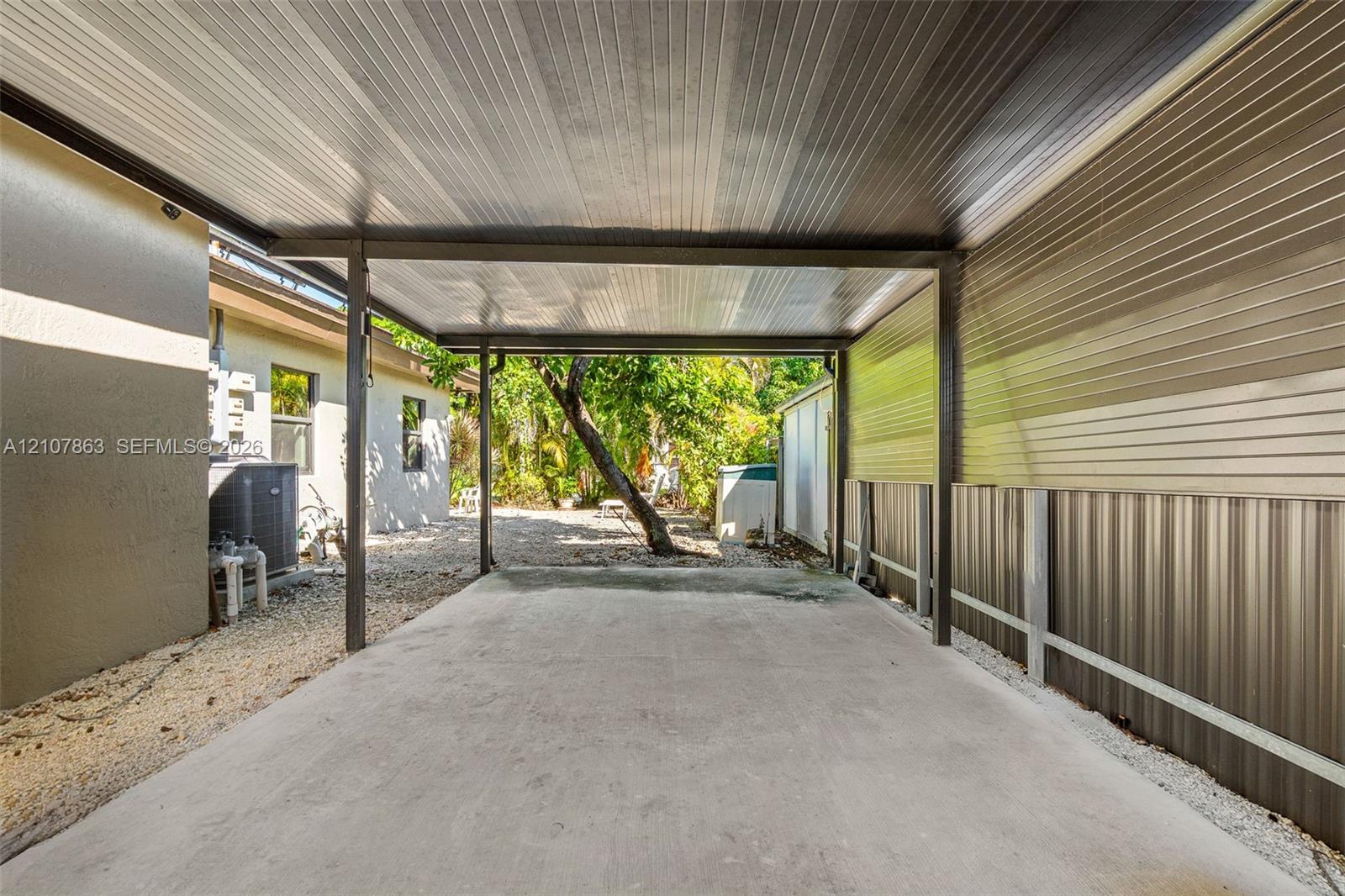 Covered carport featuring a concrete parking surface, corrugated metal wall paneling, and a metal roof structure