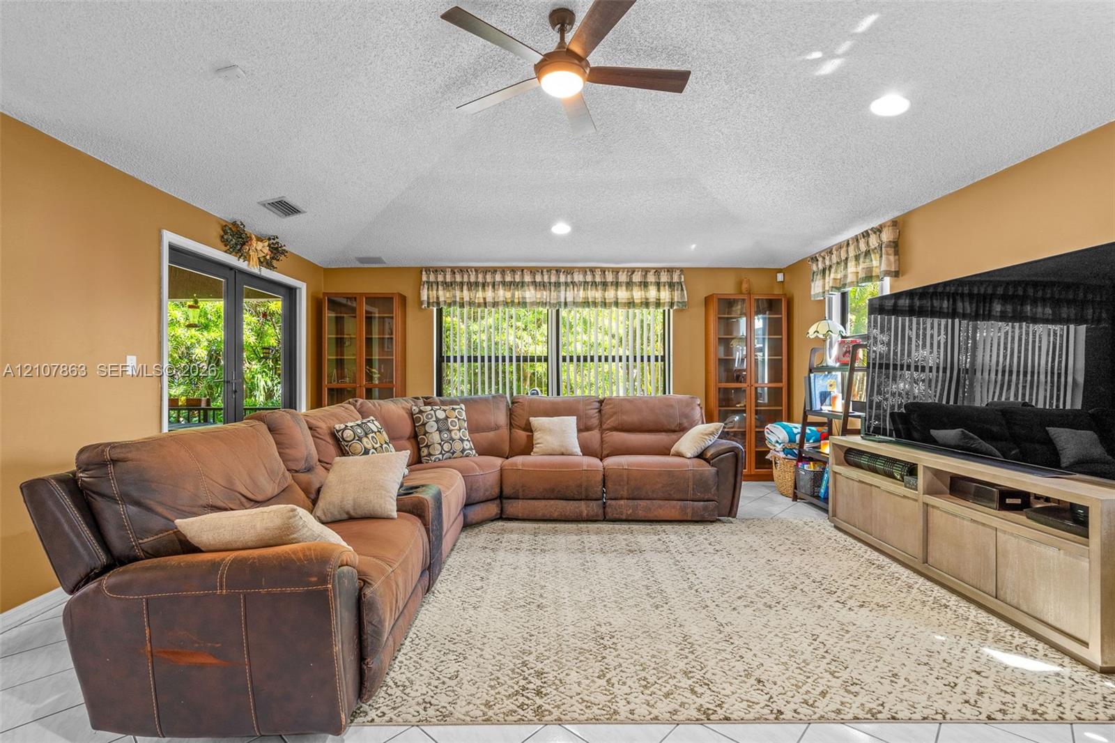 Vaulted ceilings featuring a central overhead fan, tile flooring, built-in display cabinetry, and double glass-paneled exterior doors