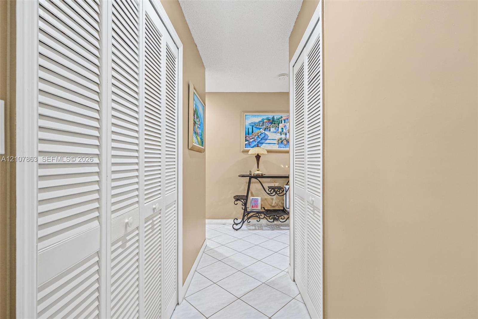 Hallway featuring white tiled flooring and dual white louvered closet doors