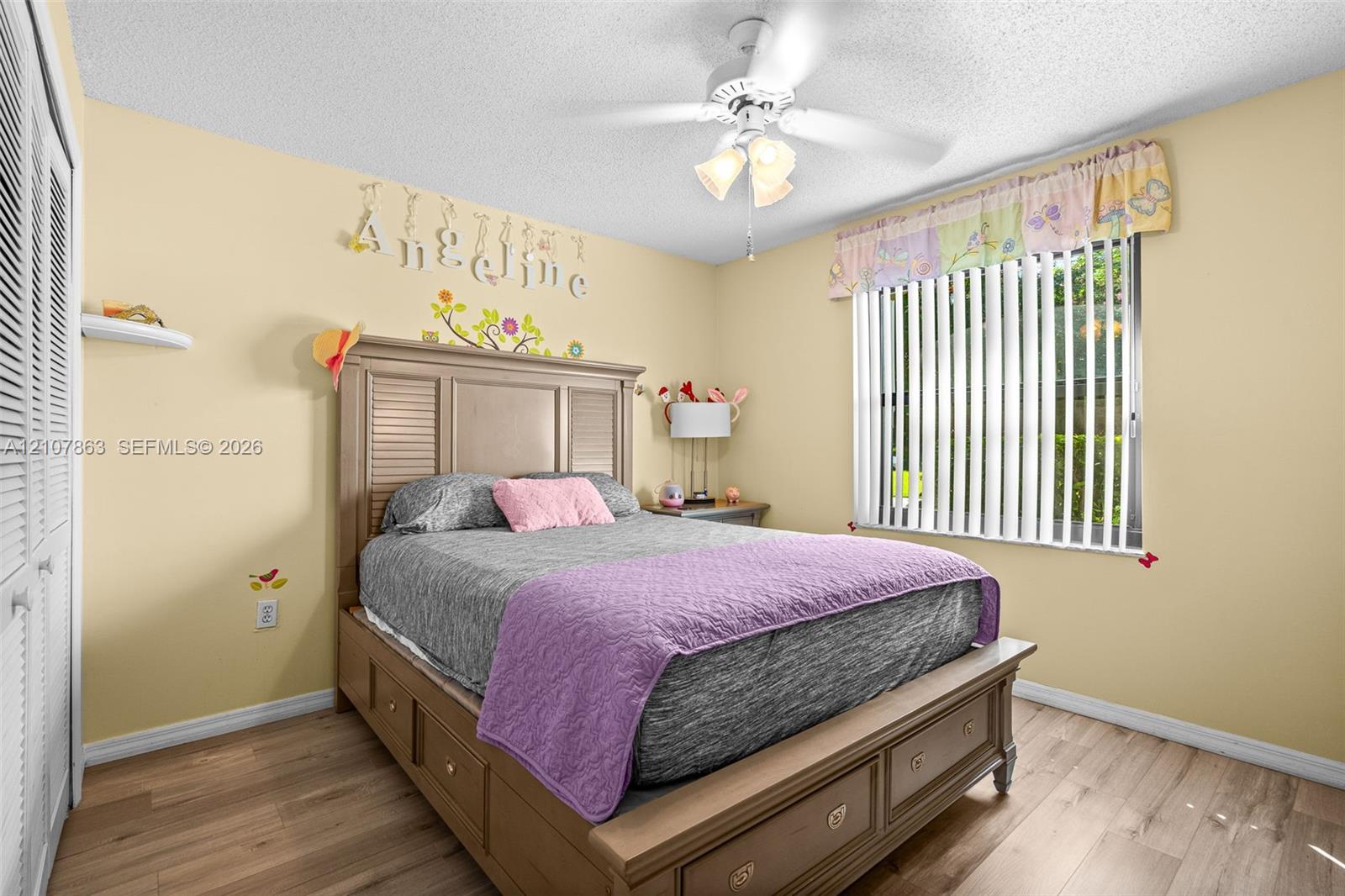 Bedroom featuring wood-finish flooring, a ceiling fan with integrated lighting, a built-in closet with louvered doors, and vertical window blinds