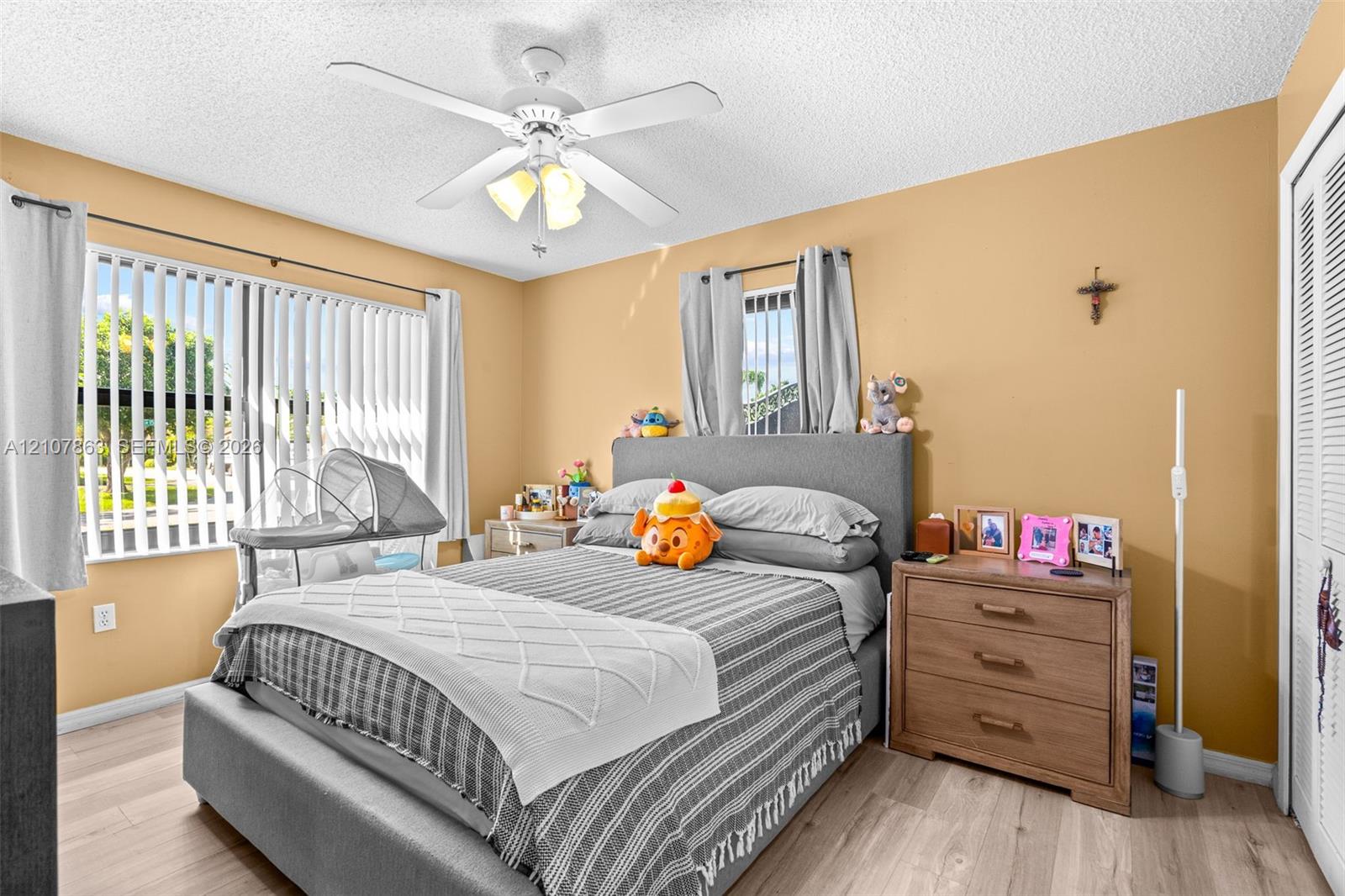 Bedroom featuring wood-finish flooring, a central ceiling fan with integrated lighting, dual-pane windows with vertical blinds, and louvered closet doors