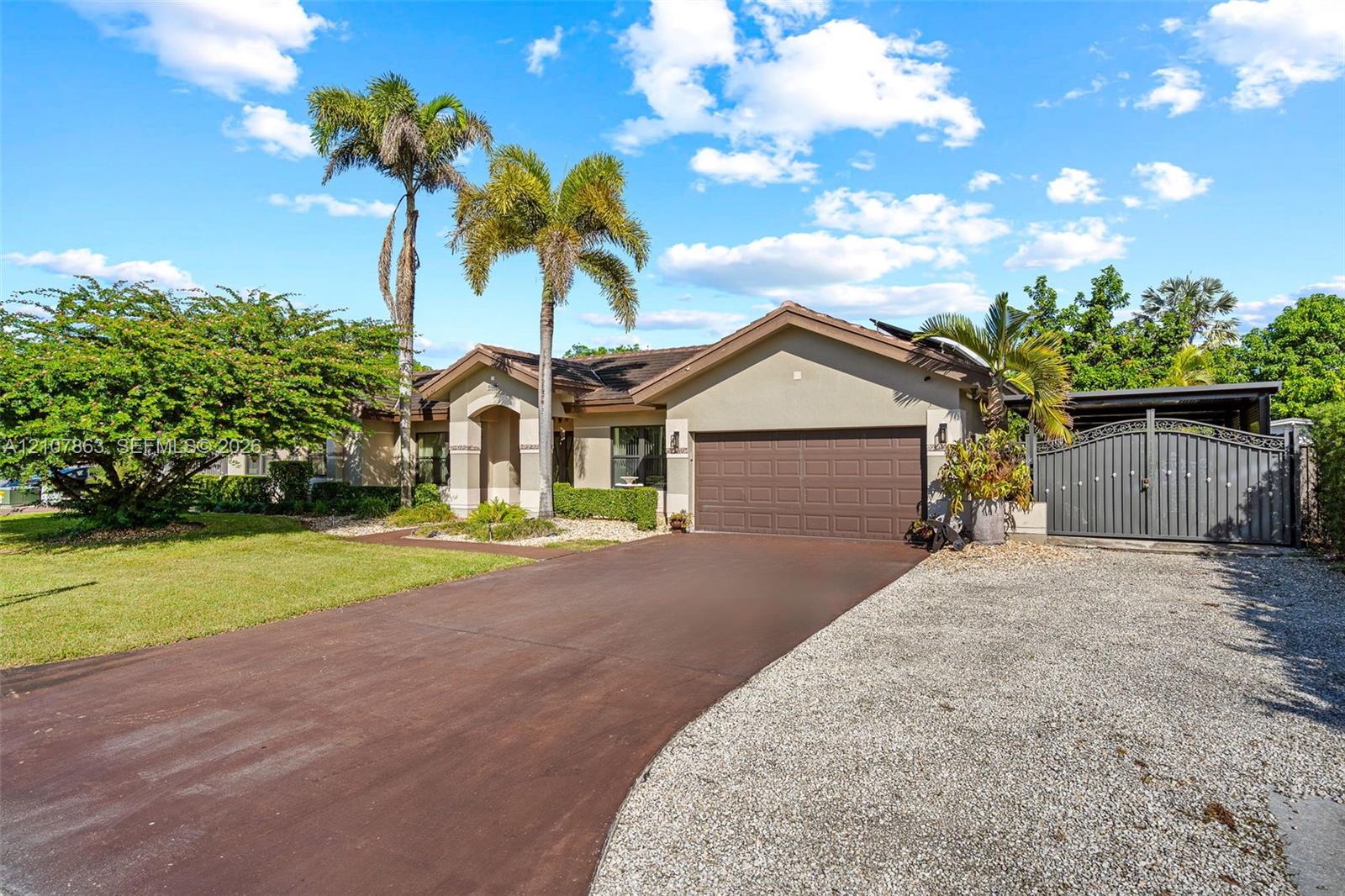 Single-story residence featuring a stucco exterior, an attached two-car garage, an asphalt driveway, a gravel parking area, and decorative metal gates Single-story residence featuring a stucco exterior, an attached two-car garage, an asphalt driveway, a gravel parking area, and decorative metal gates