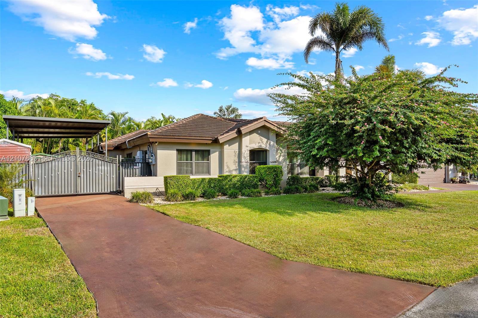 Single-story residence featuring a tile roof, paved driveway, metal gate, carport, and landscaped lawn