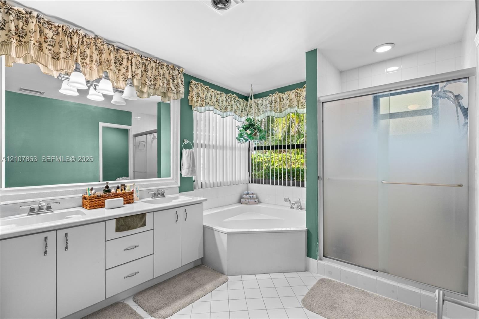 Dual-sink vanity with white cabinetry, corner soaking tub, and a glass-enclosed shower featuring tile surrounds
