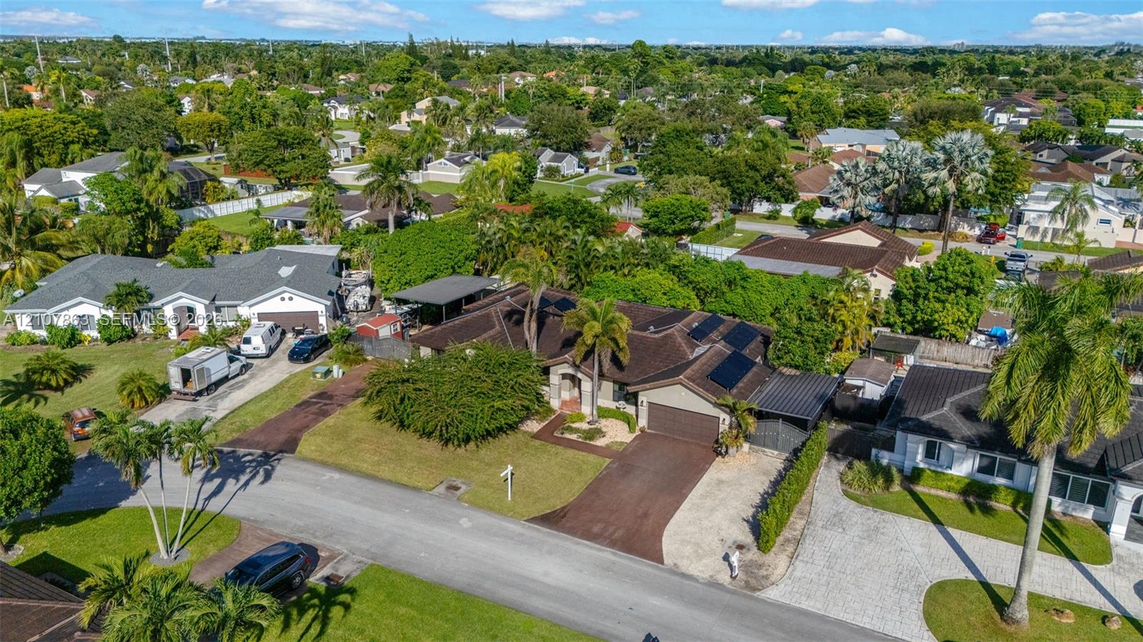 Aerial perspective of a single-story residence featuring a multi-pitched roof, roof-mounted solar panels, an integrated two-car garage, and a paved driveway