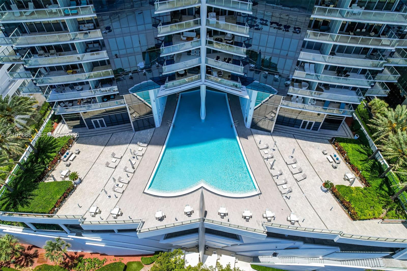 High-rise pool terrace featuring a geometric swimming pool, paved sundeck, glass-railed balconies, and landscaped grounds