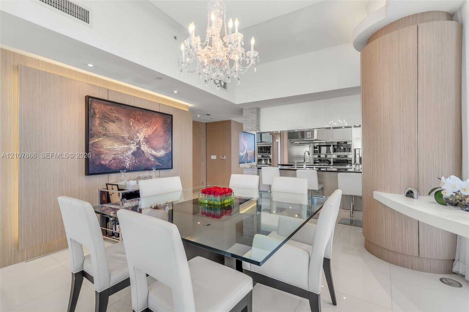 Formal dining area featuring a tiered crystal chandelier, wood-finish wall paneling, curved built-in cabinetry, and white polished flooring