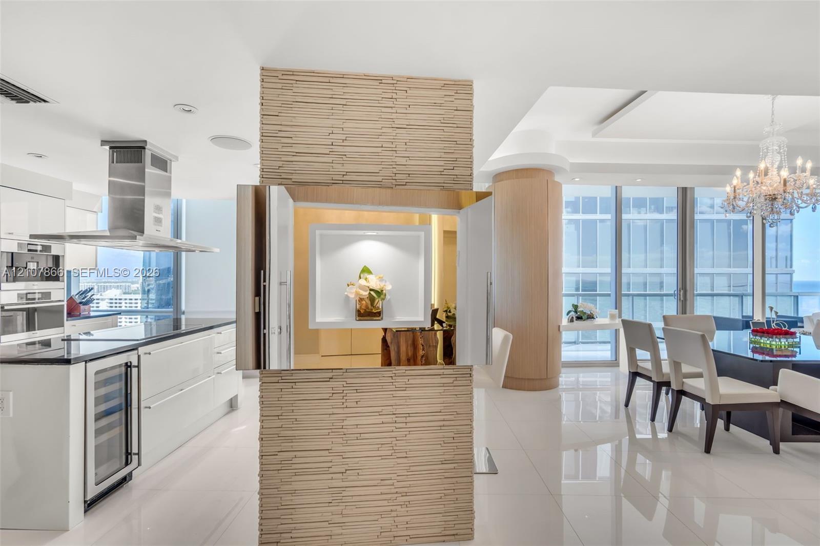 Stacked stone accent wall with a recessed display niche, white high-gloss cabinetry, stainless steel range hood, built-in wine refrigerator, and floor-to-ceiling windows