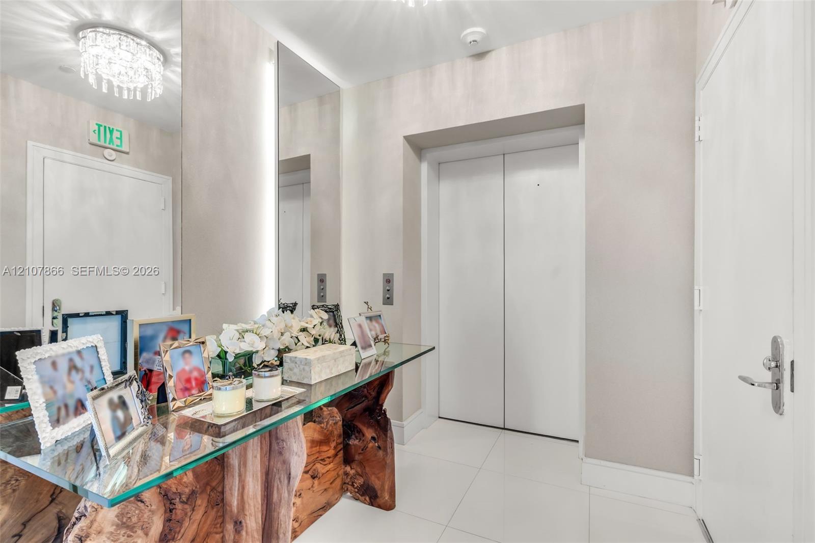 Elevator entry featuring white tile flooring, neutral wall finish, and a ceiling-mounted crystal chandelier