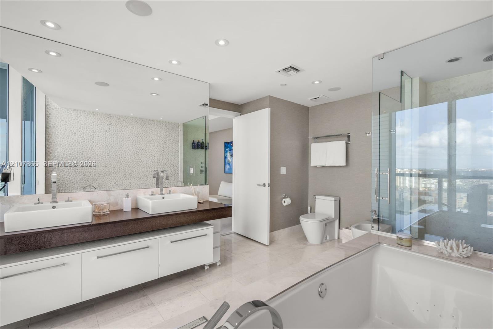 Floating double vanity with dual vessel sinks, full-width wall mirror, glass-enclosed shower, soaking tub, and stone tile flooring