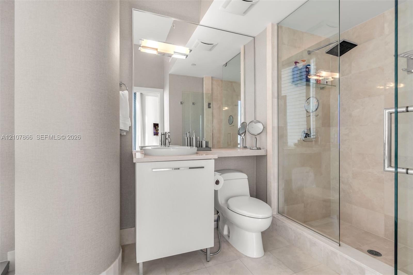 Bathroom featuring a white vanity with a vessel sink, a full-length wall mirror, a glass-enclosed walk-in shower with stone-tile surround, and a rain-style showerhead