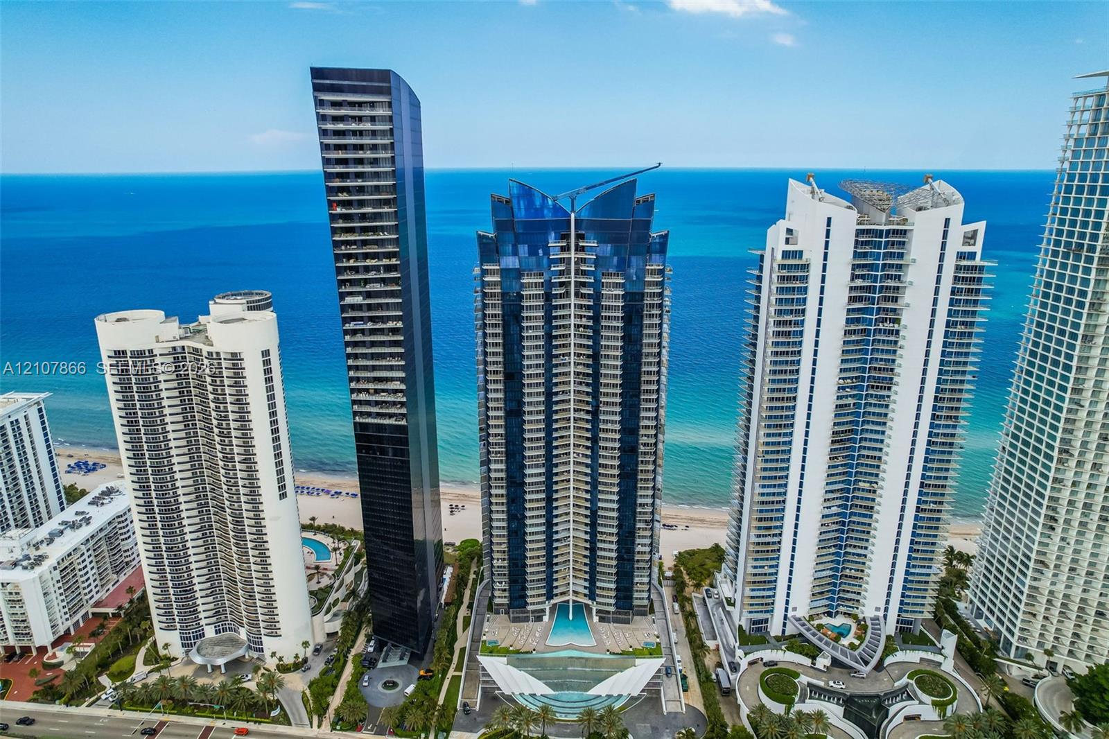 High-rise residential tower featuring a glass facade, private balconies, and an outdoor swimming pool situated along the beachfront