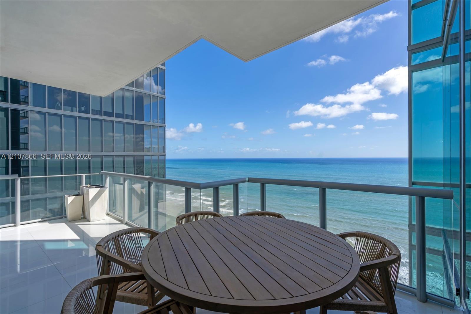 Covered balcony featuring glass paneled railings, white tile flooring, and ocean frontage