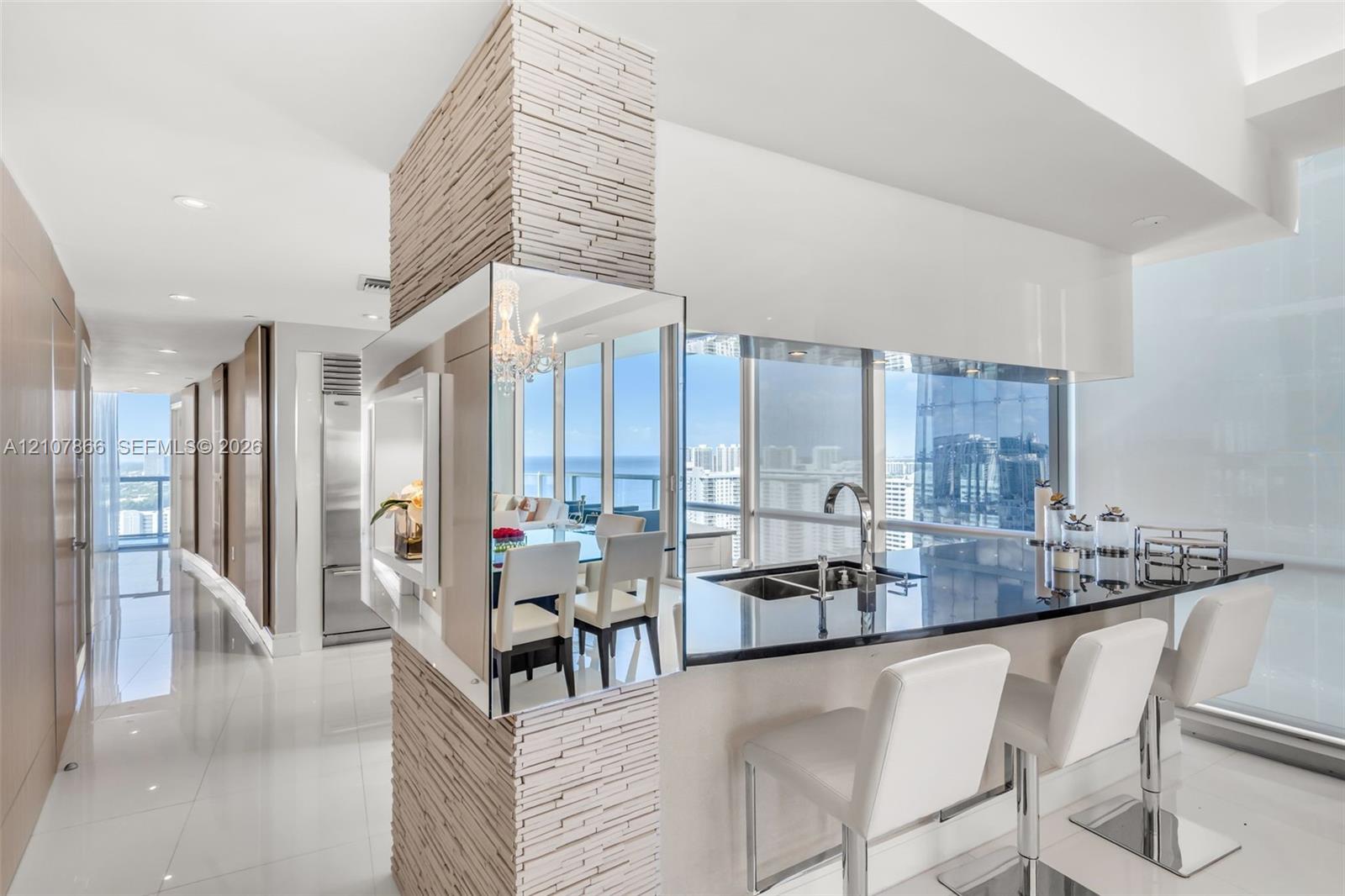 Stone-clad structural pillar, polished dark countertop, stainless steel dual-basin undermount sink, floor-to-ceiling glass windows, and glossy tile flooring