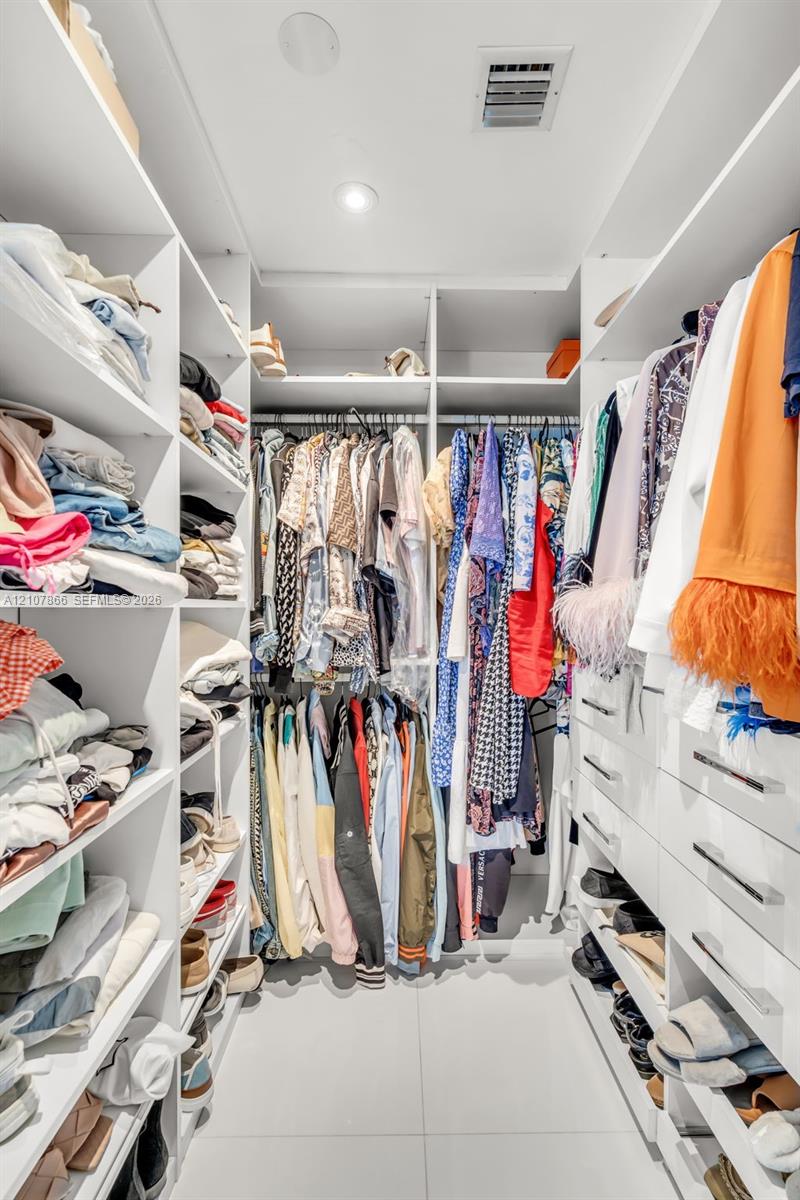 Custom walk-in closet featuring extensive white built-in cabinetry, tiered shelving, integrated hanging rods, recessed lighting, and large-format tile flooring
