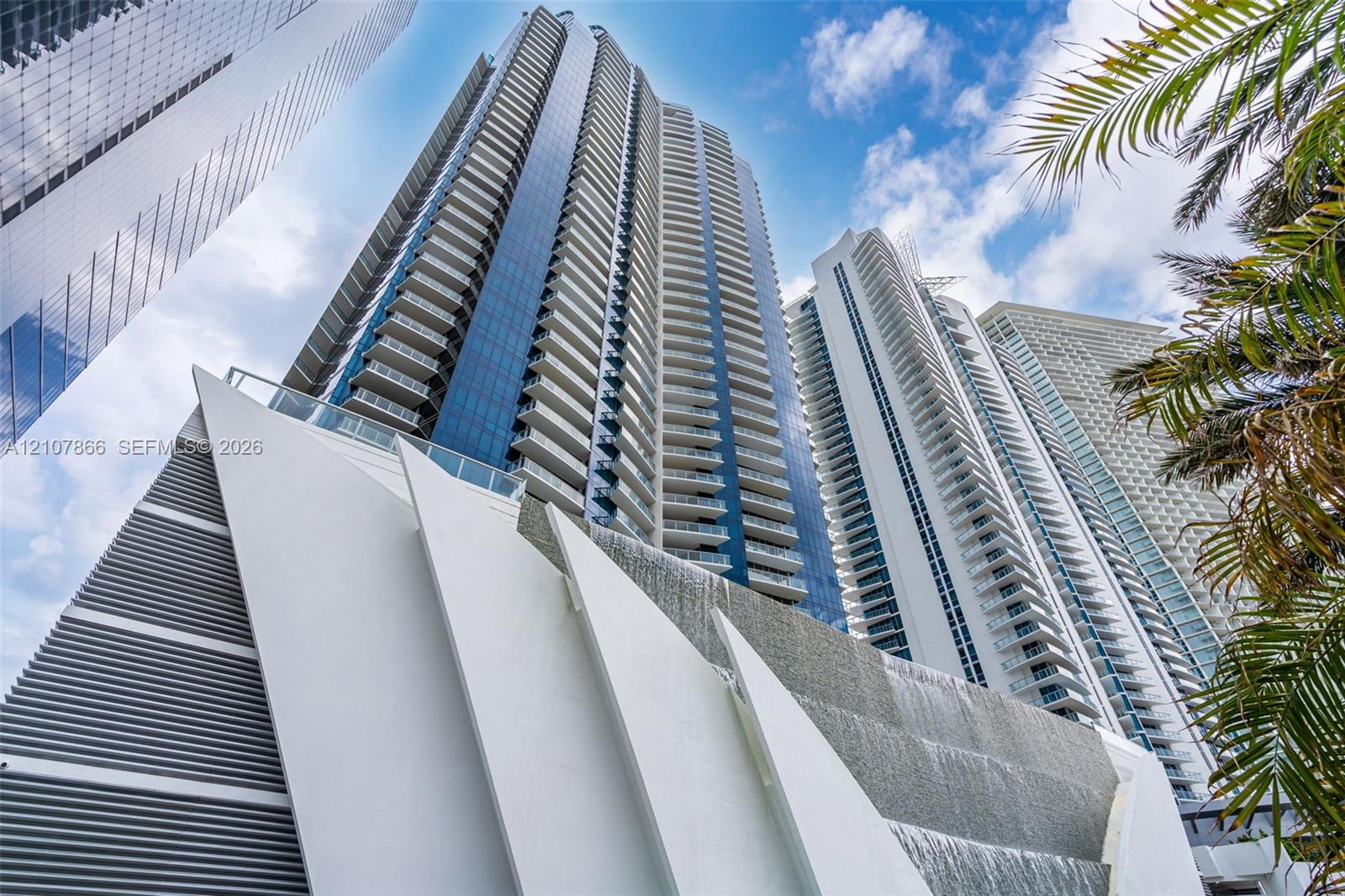 High-rise architectural exterior featuring glass curtain walls, private balconies with glass railings, and a tiered water feature