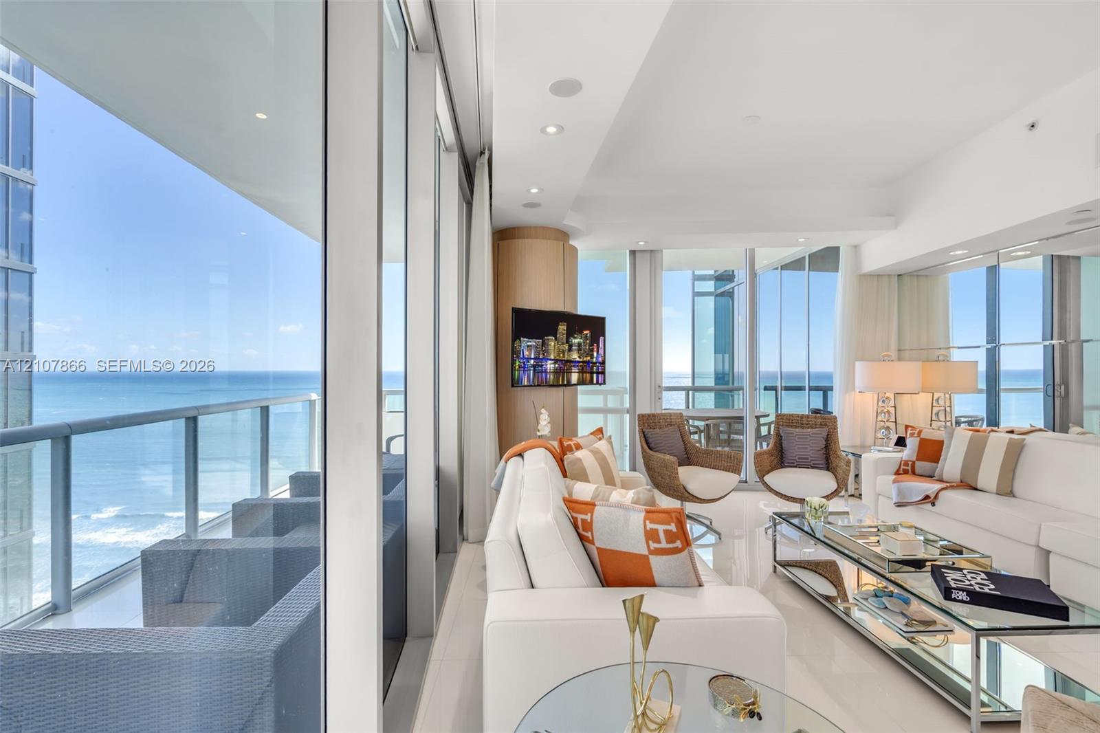 Floor-to-ceiling glass walls, expansive private balcony with metal railing, polished stone flooring, recessed ceiling lighting, and built-in rounded cabinetry