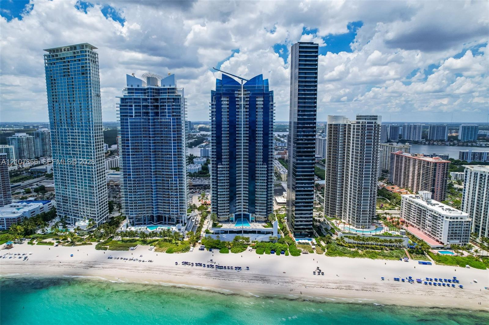 High-rise coastal development featuring glass-paneled architecture, direct oceanfront access, extensive white sand shoreline, and ground-level pool facilities