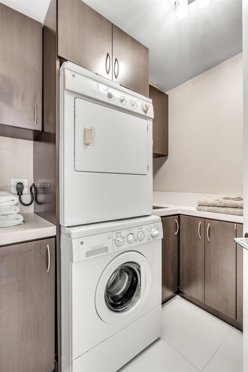 Laundry area featuring floor-to-ceiling dark-finish cabinetry, stacked washer and dryer unit, solid-surface countertops, and an integrated basin