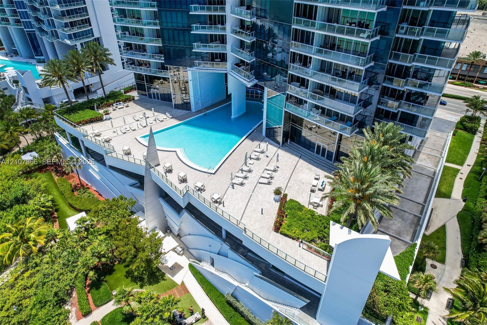 High-rise complex featuring an expansive elevated pool terrace, glass-railing balconies, stone-paver decking, and landscaped green spaces