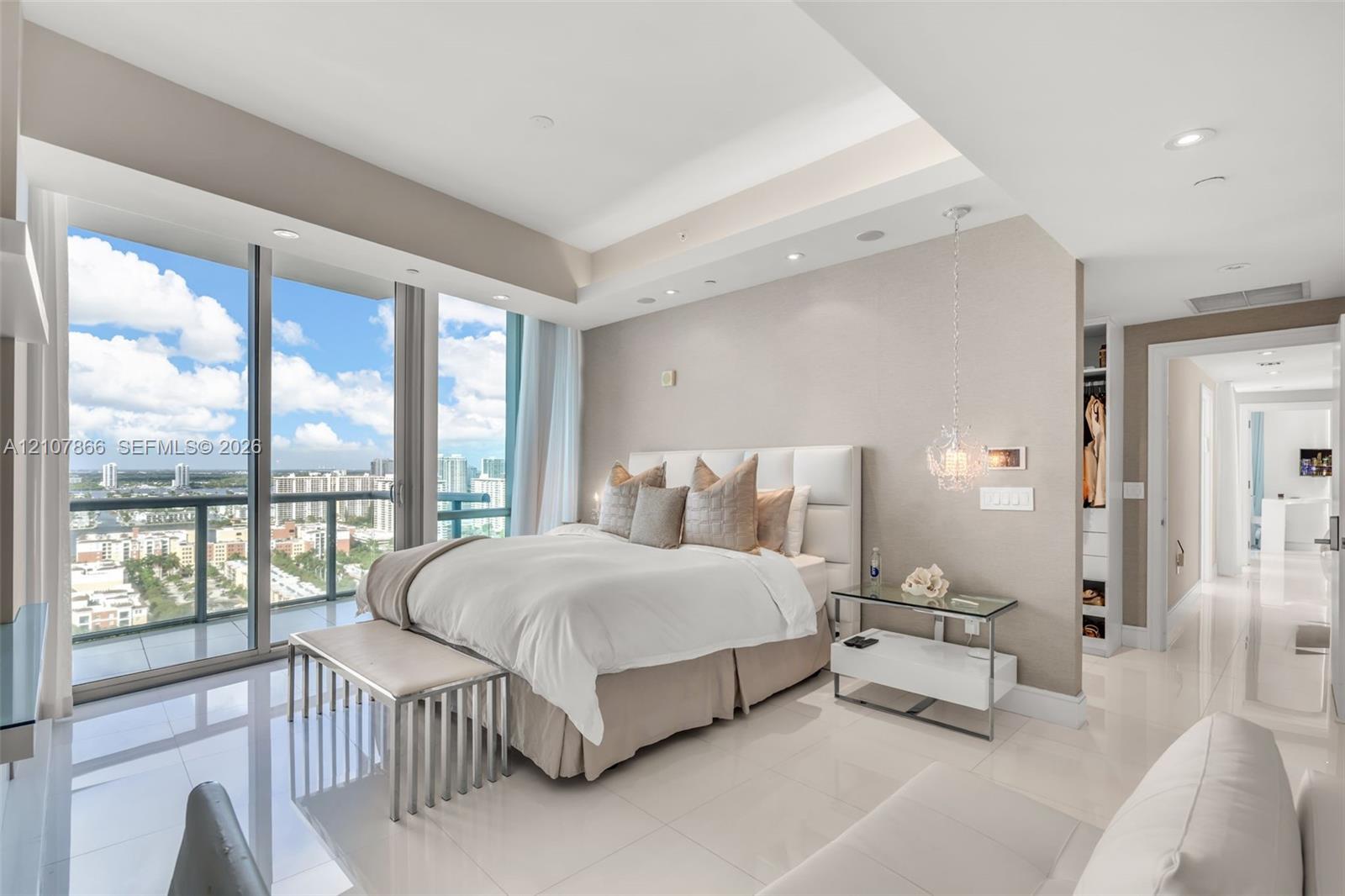 Floor-to-ceiling glass sliding doors, tray ceilings with recessed lighting, polished porcelain tile flooring, textured wall finishes, and a dedicated walk-in closet with custom built-in shelving