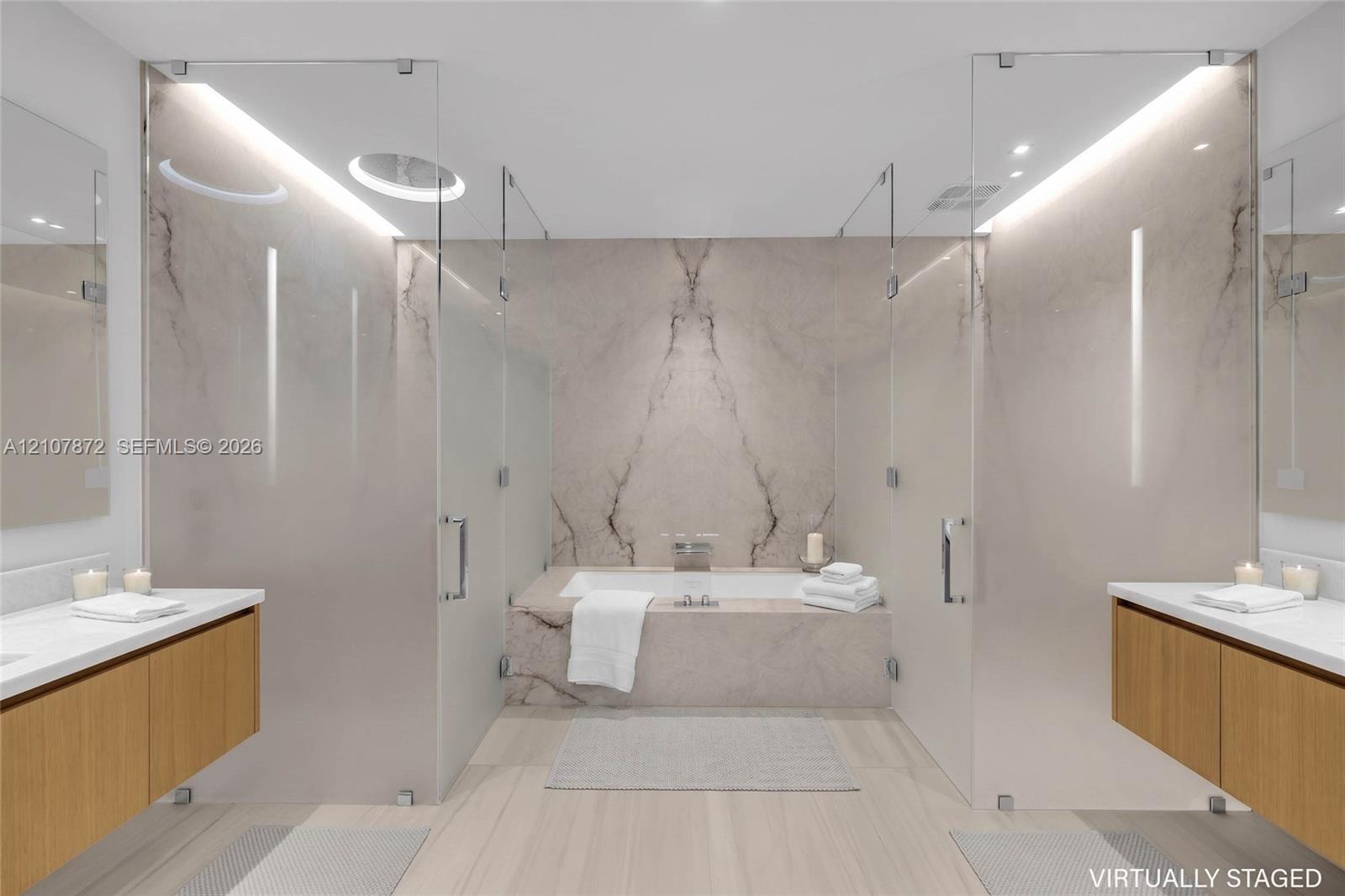 Dual floating wood-finish vanities with rectangular integrated sinks, stone-clad drop-in bathtub with wall-mounted faucet, full-height stone backsplash, and frameless glass-enclosed shower stalls with recessed overhead lighting
