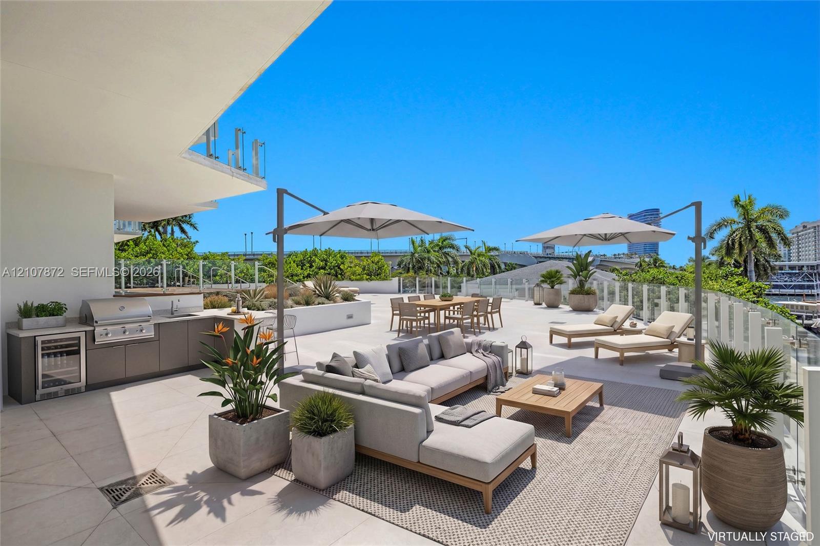 Expansive outdoor terrace featuring stone-tiled flooring, a built-in outdoor kitchen with stainless steel appliances, a bar refrigerator, and glass panel railing