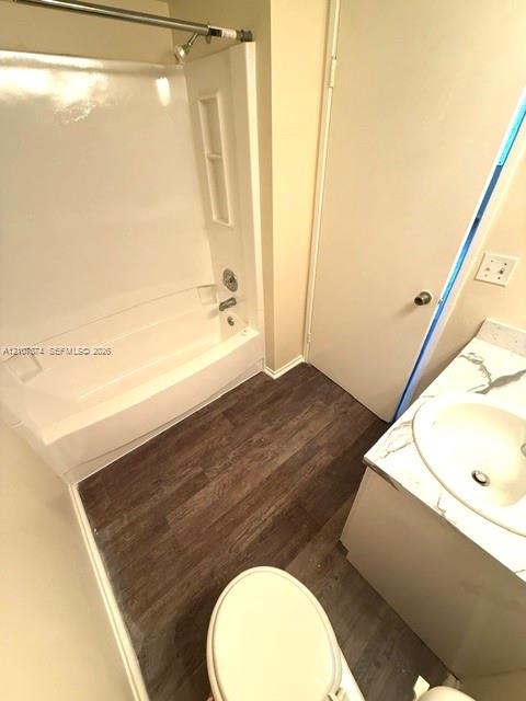 Bathroom featuring wood-finish flooring, a white bathtub and shower surround, and a vanity topped with a stone-finish counter and integrated sink