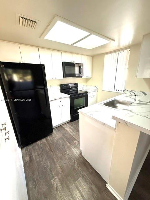 Kitchen featuring white cabinetry, stone-finish countertops, black appliances, a stainless steel sink, and wood-finish flooring