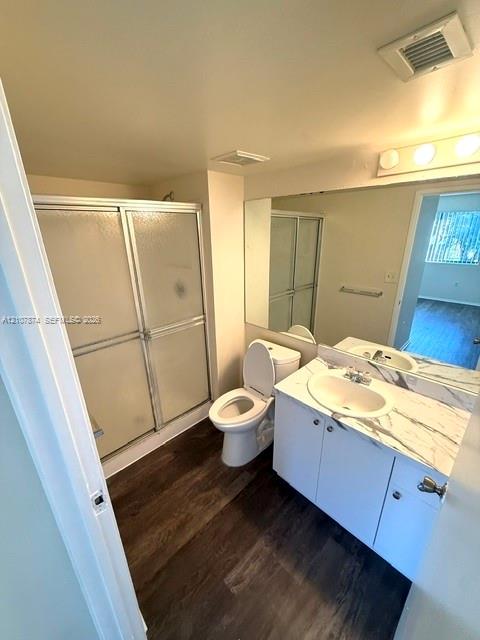 Bathroom featuring white cabinetry, stone-finish vanity countertop with an integrated oval basin, full-width wall mirror, wood-finish flooring, and a glass-enclosed shower