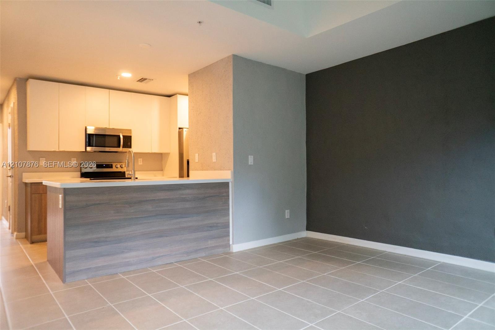 Kitchen featuring white flat-panel cabinetry, light-toned stone-surface countertops, stainless steel appliances, a wood-finish peninsula, and large-format tile flooring