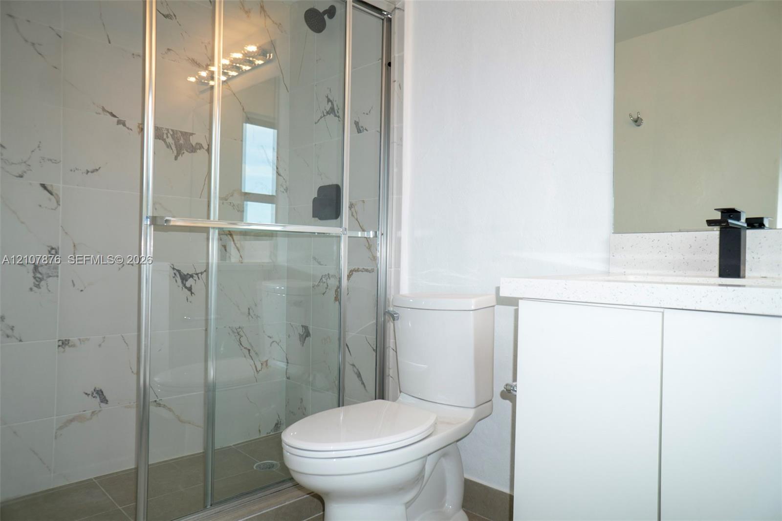 Shower featuring a glass enclosure and patterned wall tile, complemented by a white vanity with a solid surface countertop and a matte black faucet