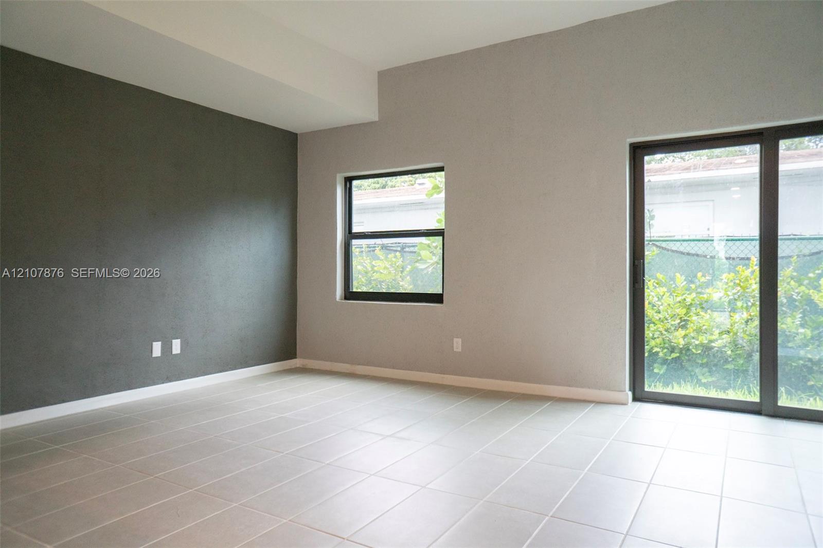 Room featuring ceramic tile flooring, a charcoal-colored accent wall, neutral wall paint, a rectangular window, and a sliding glass door