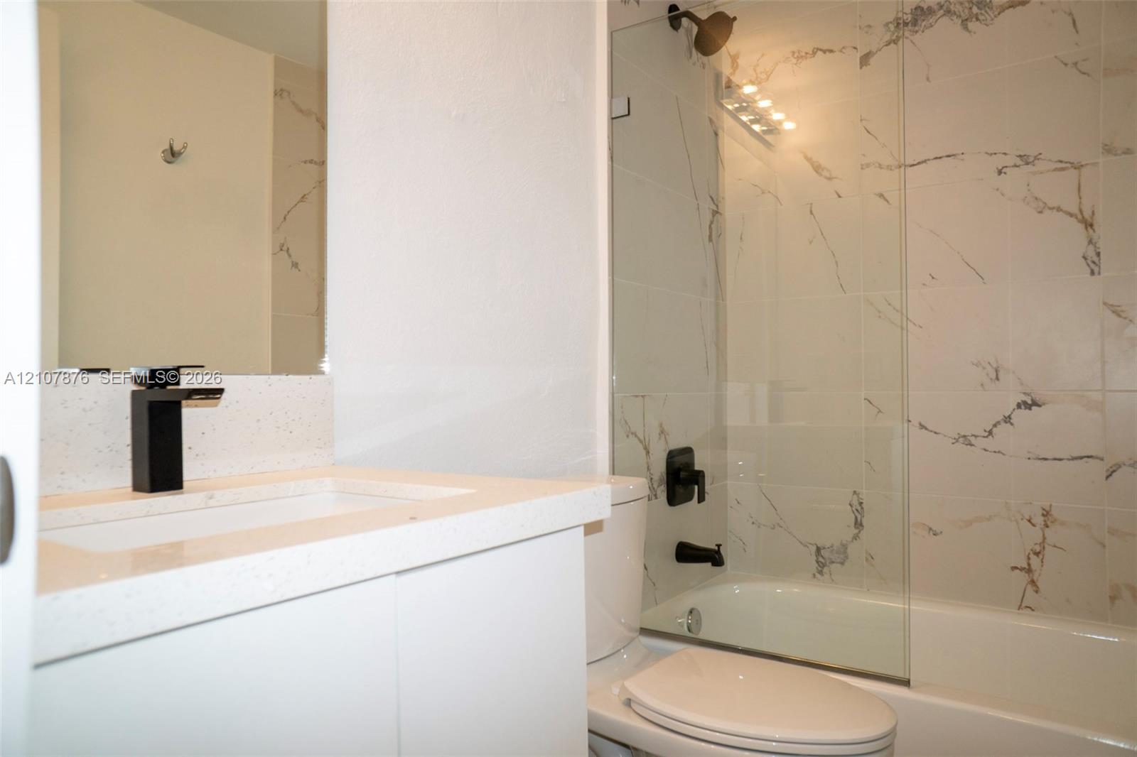 Bathroom featuring a white vanity with a quartz countertop, matte black faucet, shower enclosure with floor-to-ceiling tile, and a glass shower panel