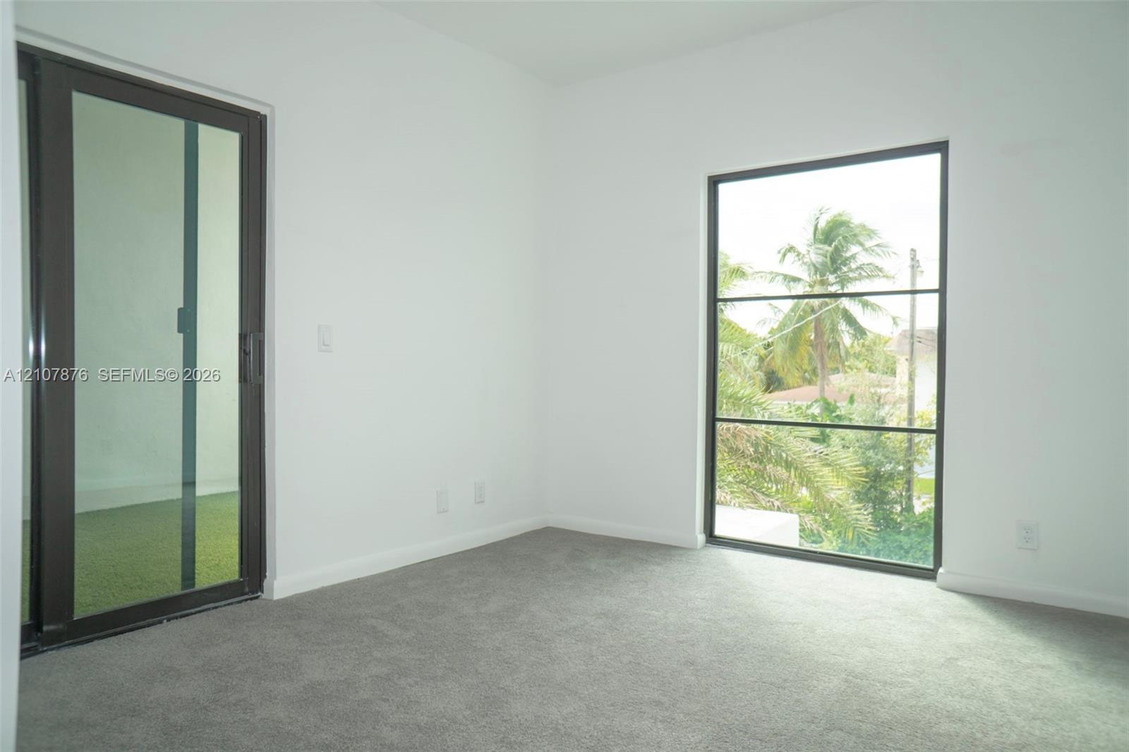 Neutral-toned carpeting, full-height sliding glass door, and large rectangular window with dark-finish frames