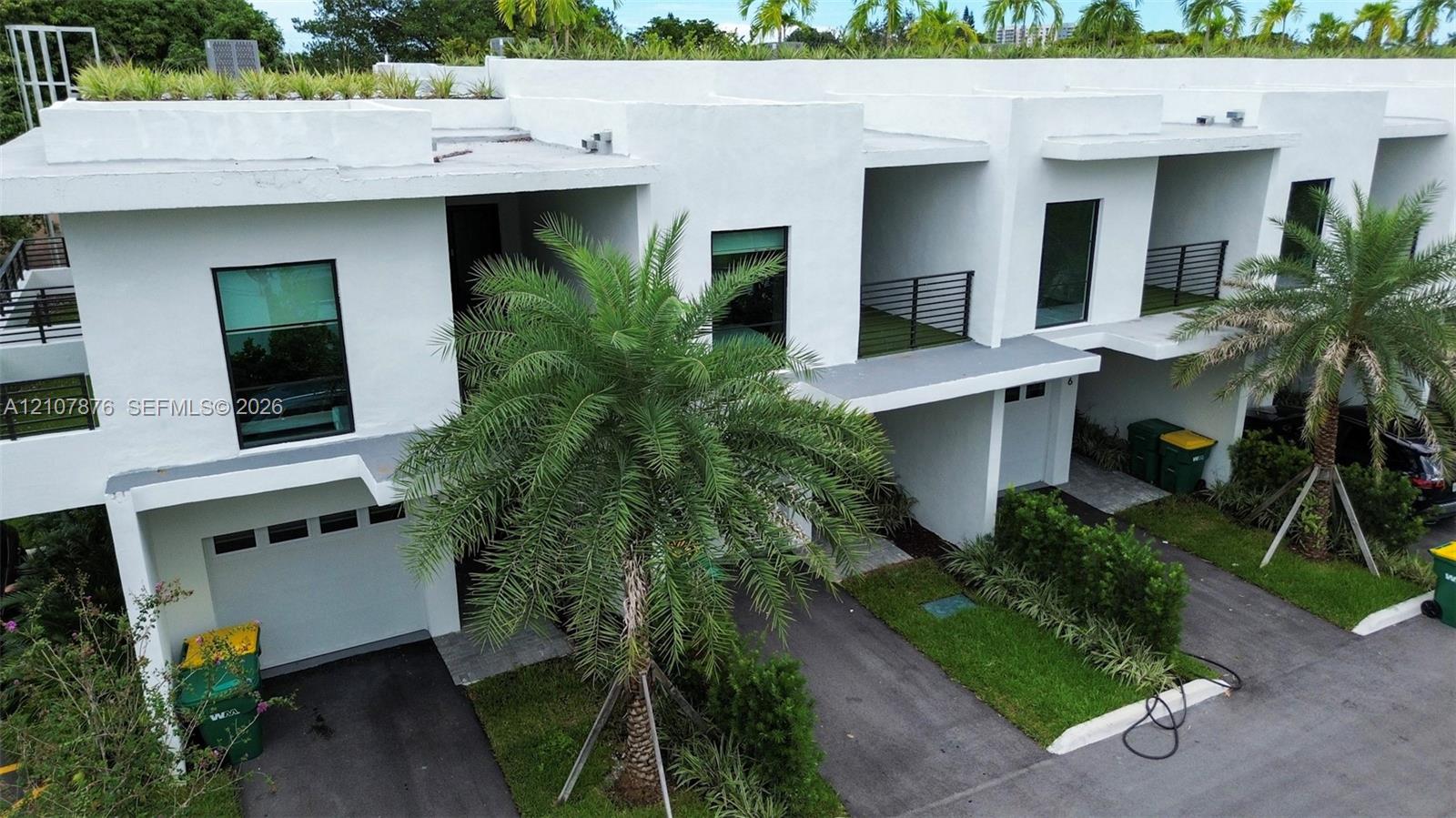 Modern architectural exterior featuring white stucco facade, second-story balconies with horizontal railing, private garages, and integrated rooftop landscaping