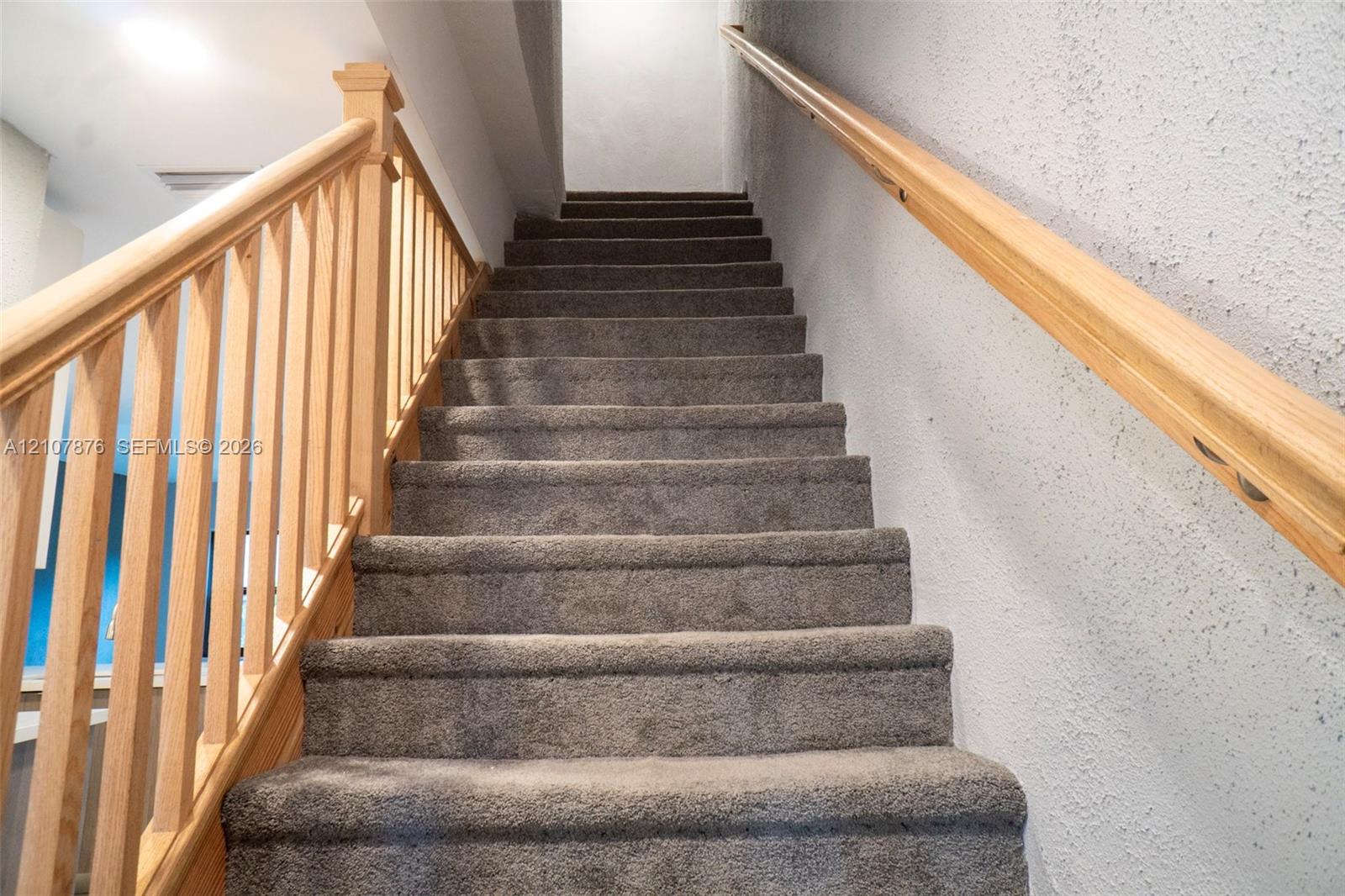 Staircase featuring wall-to-wall carpeting, light-tone wood balusters, a matching wood handrail, and textured wall finishes