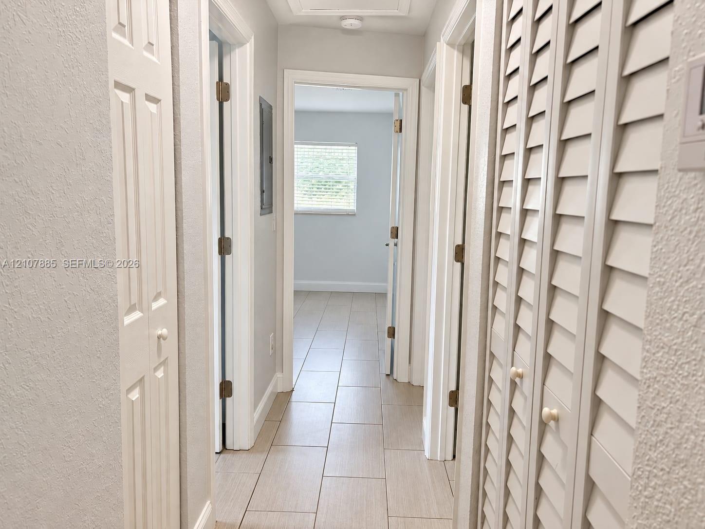 Hallway featuring neutral-toned tile flooring, louvered closet doors, and multiple interior doorways
