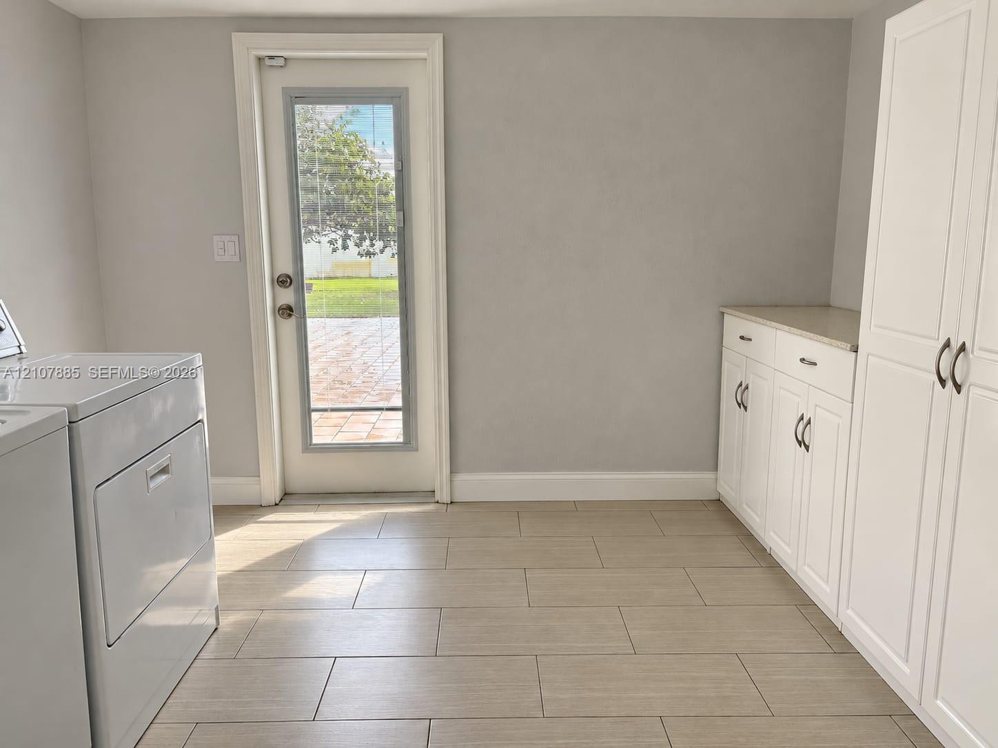 Utility space featuring light-toned tile flooring, built-in white cabinetry with stone countertops, and a glass-paneled exterior door